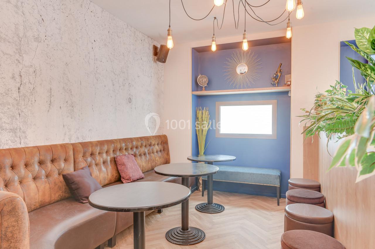 Banquette en cuir, tables rondes et décoration murale dans un espace lumineux avec un mur bleu et des plantes.