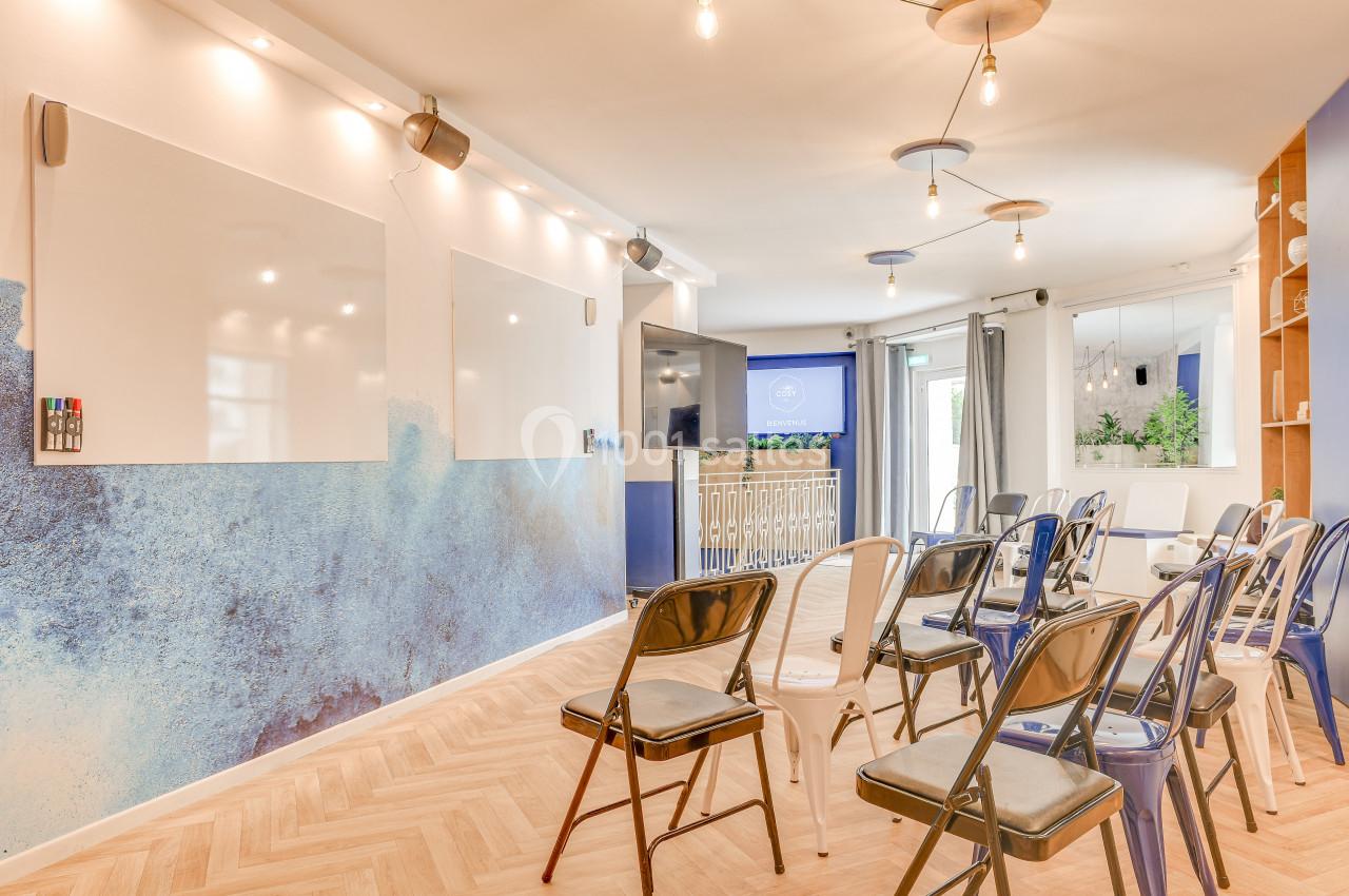 Salle lumineuse avec chaises disposées face à des tableaux blancs, décorée de tons bleus et éclairée par des suspensions.