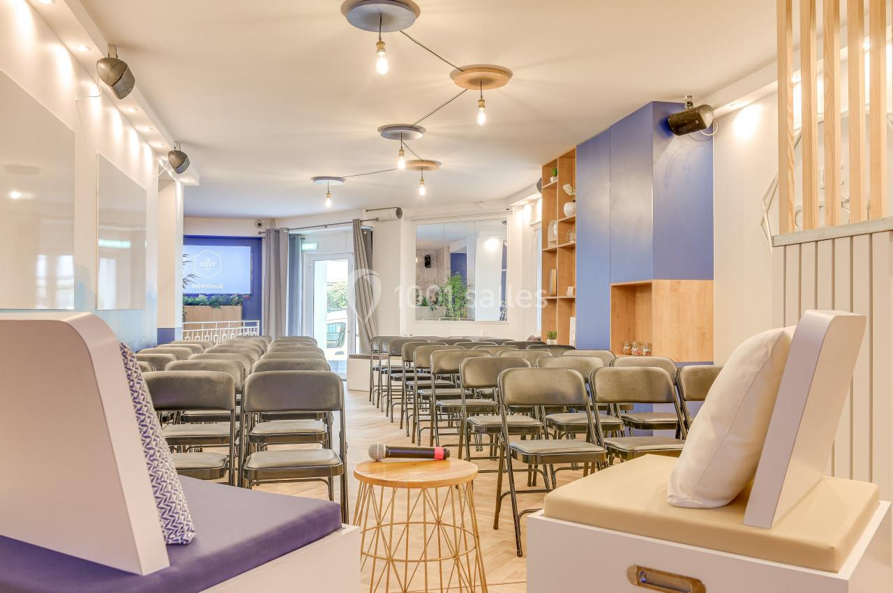 Salle lumineuse aménagée avec des chaises alignées, un micro sur une table basse et des éléments décoratifs modernes.