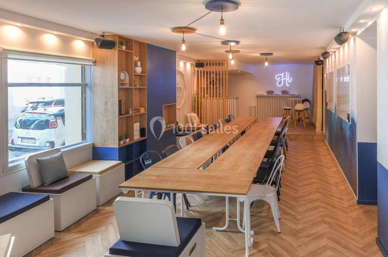 Salle lumineuse avec grande table en bois, chaises colorées, parquet en chevrons et décoration moderne.