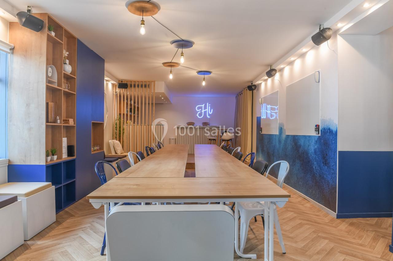 Salle de réunion lumineuse avec une grande table en bois, chaises variées, décor moderne et éclairage suspendu.