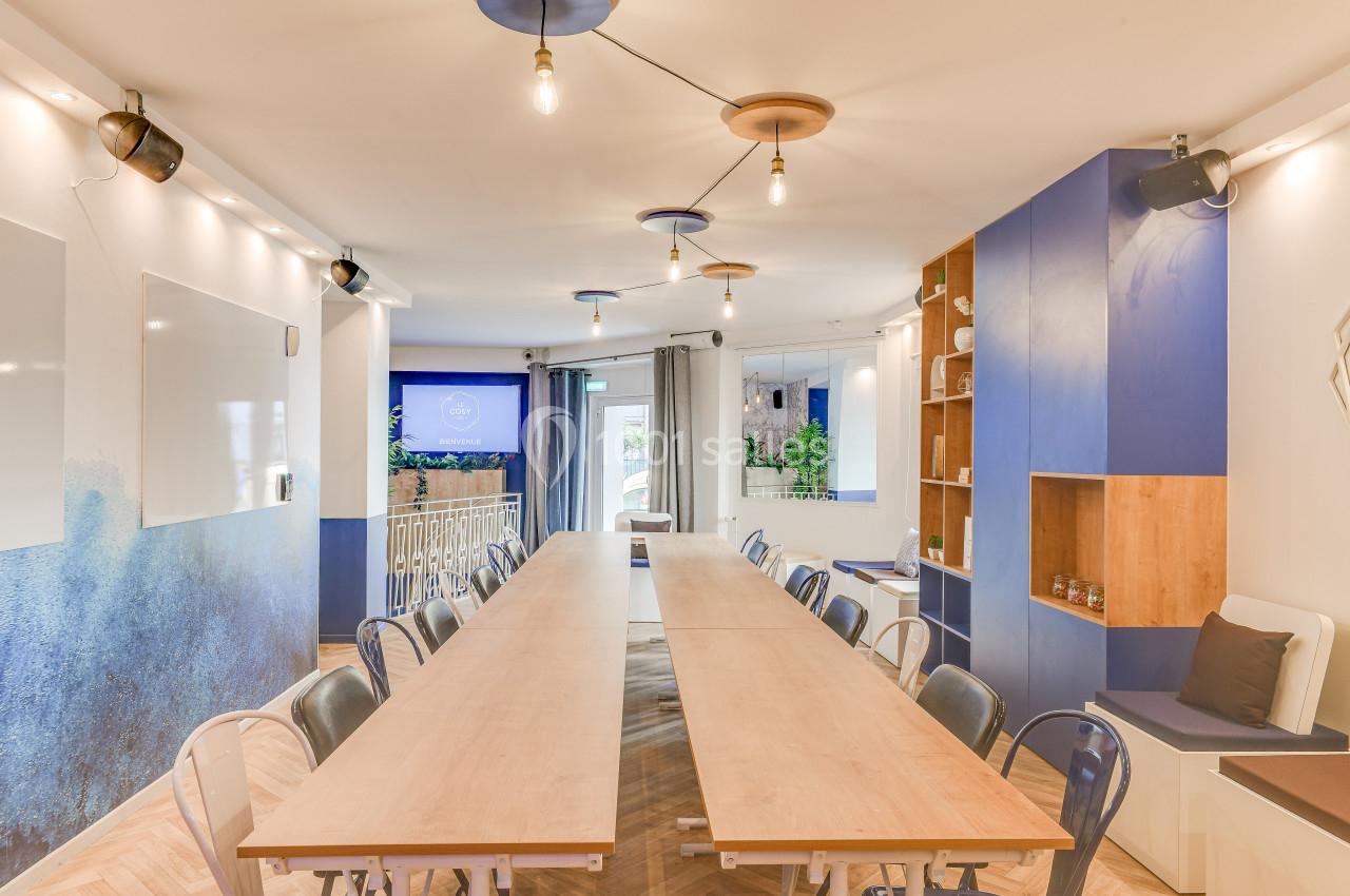 Salle de réunion lumineuse avec une grande table en bois, des chaises, des murs bleus et des étagères intégrées.