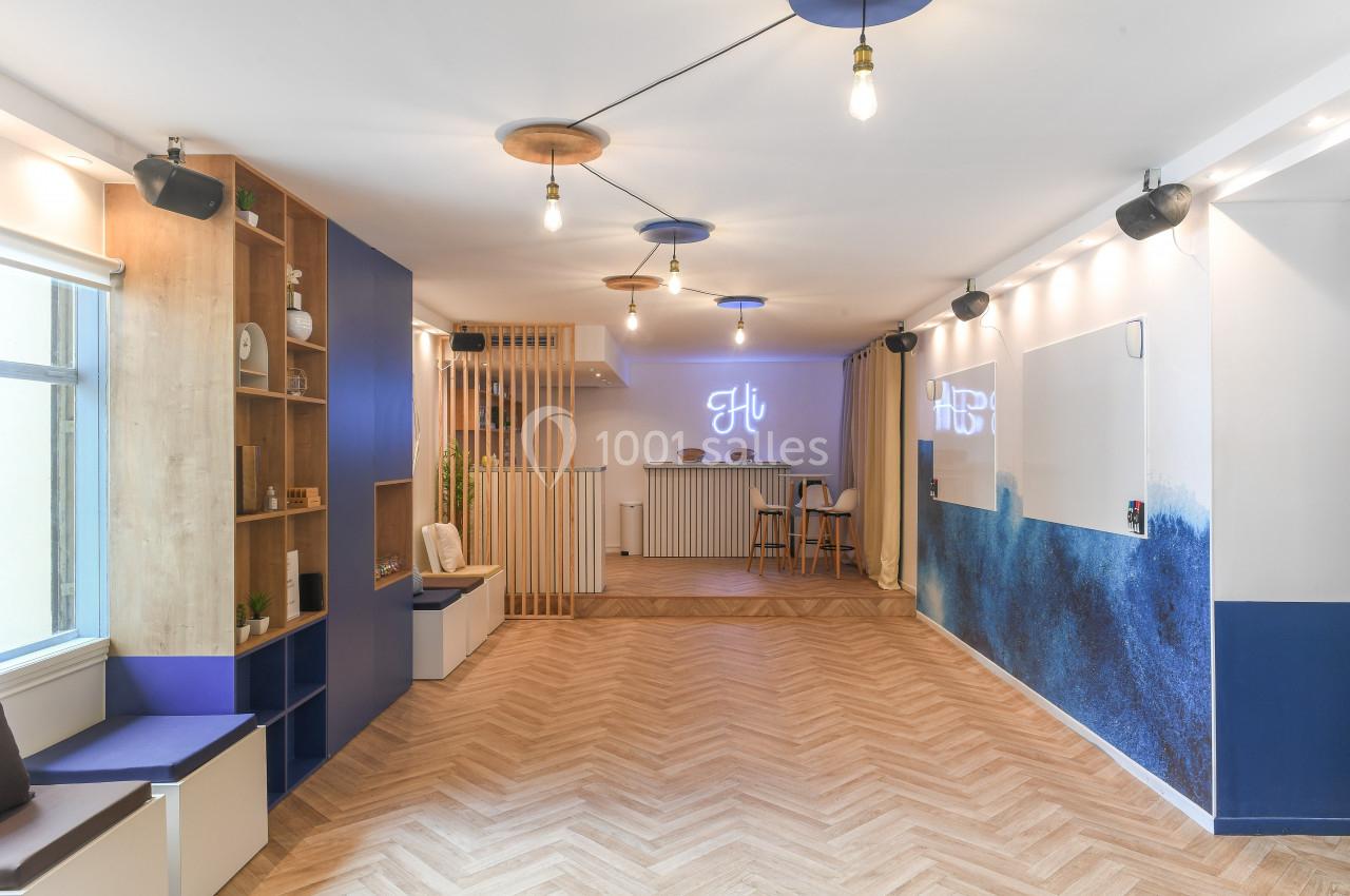 Salle lumineuse avec parquet en chevrons, murs décorés de bleu et blanc, et espace d'accueil au fond.