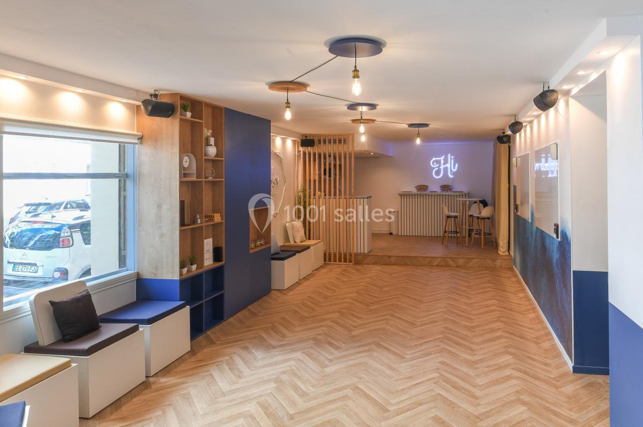 Salle lumineuse avec parquet en chevrons, banquettes près d'une fenêtre, et comptoir avec enseigne lumineuse au fond.