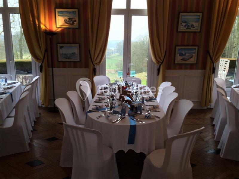 Salle de réception élégante avec des tables dressées, nappes blanches et vue sur un paysage extérieur verdoyant.