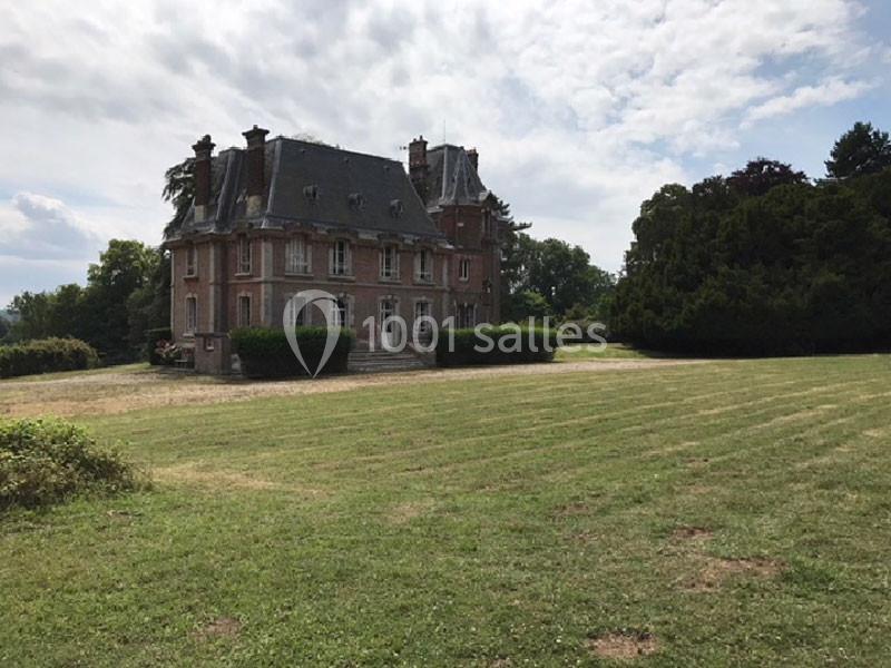 Manoir en briques rouges entouré d'un grand jardin avec pelouse, sous un ciel partiellement nuageux.