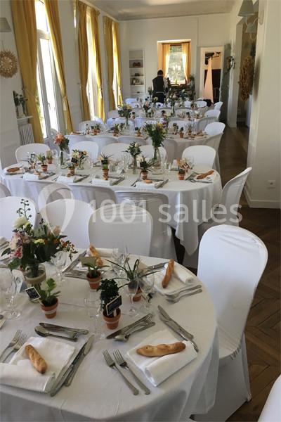 Salle de réception décorée avec des tables rondes dressées, nappes blanches, fleurs et couverts disposés élégamment.