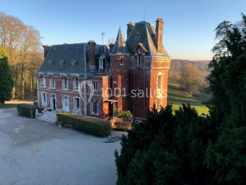 Manoir en briques rouges avec toit en ardoise, entouré de verdure et baigné par une lumière de fin de journée.