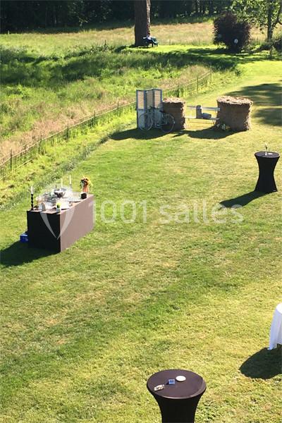Espace extérieur avec tables hautes noires, comptoir de service et décor champêtre sur une pelouse ensoleillée.