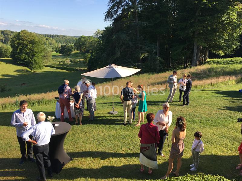 Groupe de personnes discutant en plein air sur une pelouse avec vue sur un paysage verdoyant et un parasol.