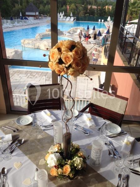 Centre de table floral avec des roses jaunes et blanches, disposé sur une table dressée près d'une piscine extérieure.