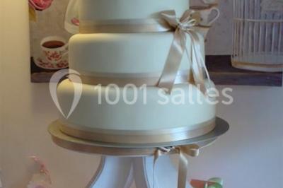 Gâteau de mariage à quatre étages décoré de rubans beige clair, posé sur un présentoir blanc.