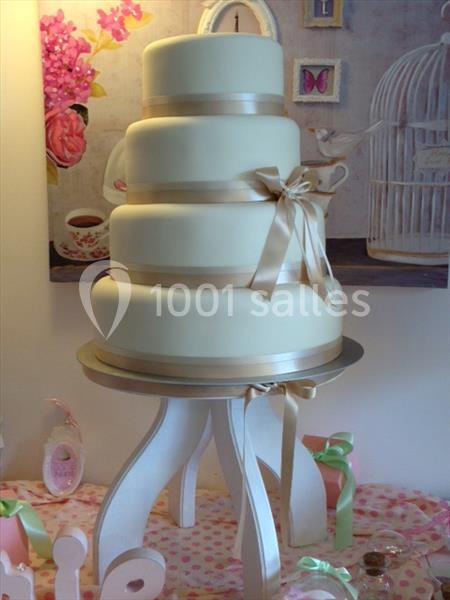 Gâteau de mariage à quatre étages décoré de rubans beige clair, posé sur un présentoir blanc.