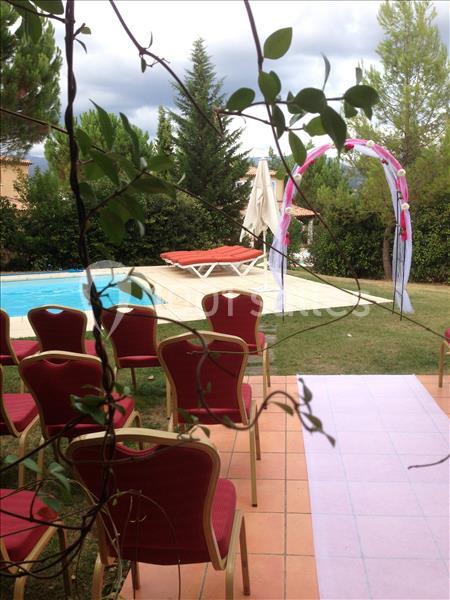 Chaises rouges alignées près d'une piscine, avec un arc décoratif et des parasols dans un jardin verdoyant.