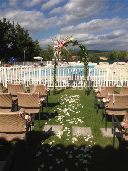 Allée décorée de pétales de fleurs menant à une arche florale devant une piscine en plein air, sous un ciel partiellement…