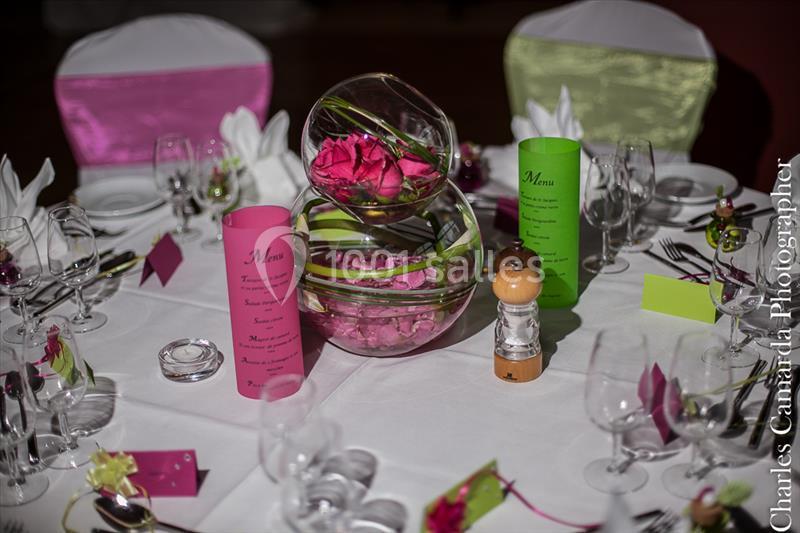 Table dressée pour un événement, avec menus colorés, verres, serviettes pliées et centre de table floral.