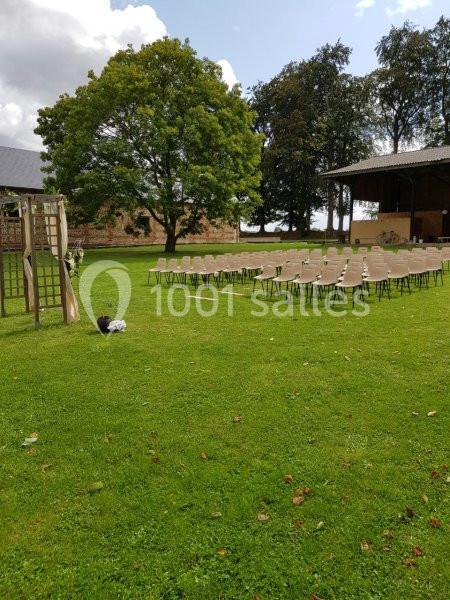 Chaises disposées en rangées sur une pelouse pour une cérémonie en plein air, avec un arbre et une pergola en arrière-plan.
