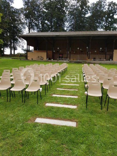 Chaises alignées en plein air sur une pelouse, face à une scène couverte en bois entourée d'arbres.