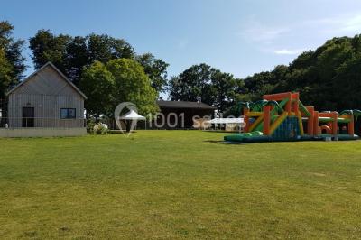Paysage champêtre avec pelouse verdoyante, arbres en arrière-plan et buissons fleuris sous un ciel bleu dégagé.