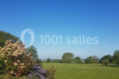 Paysage champêtre avec pelouse verdoyante, arbres en arrière-plan et buissons fleuris sous un ciel bleu dégagé.