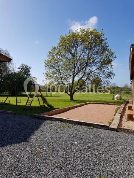Jardin avec pelouse, arbre central, balançoire en bois et terrain sablé, entouré de bâtiments et ciel dégagé.
