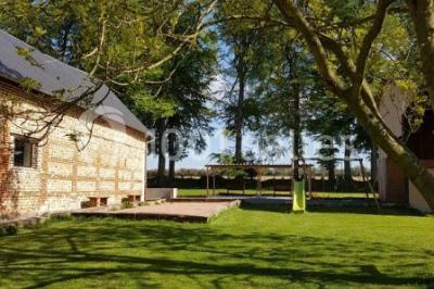 Paysage champêtre avec pelouse verdoyante, arbres en arrière-plan et buissons fleuris sous un ciel bleu dégagé.