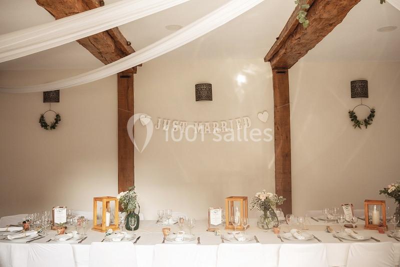 Salle décorée pour un mariage avec une table dressée, des fleurs, des lanternes et une bannière ’Just Married’.