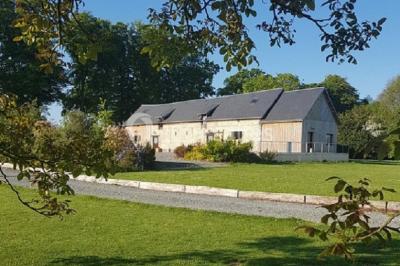 Paysage champêtre avec pelouse verdoyante, arbres en arrière-plan et buissons fleuris sous un ciel bleu dégagé.