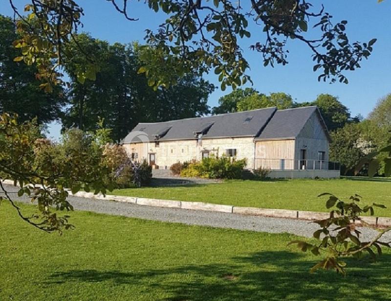 Bâtiment en pierre et bois entouré de pelouse et d'arbres sous un ciel bleu clair.