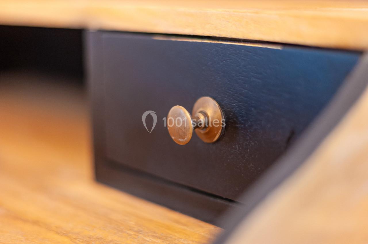 Gros plan sur un tiroir en bois noir avec une poignée ronde en métal doré, intégré dans un meuble en bois clair.