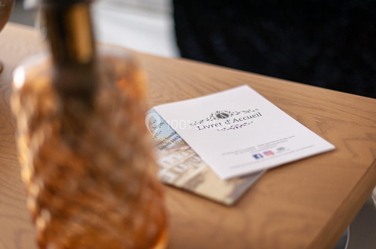 Livret d'accueil posé sur une table en bois, à côté d'un objet décoratif en verre.