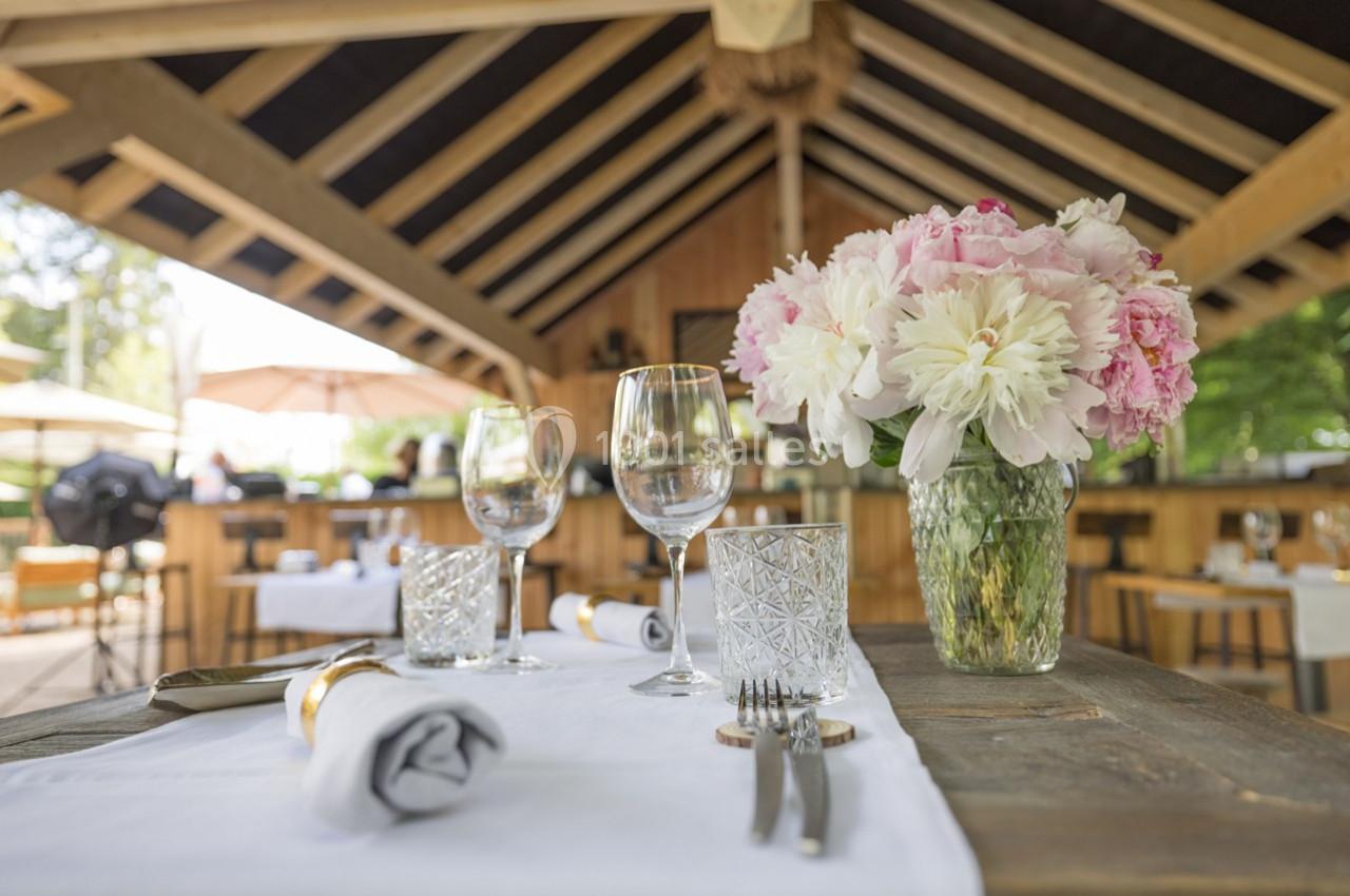 Table dressée avec élégance, contenant des verres, couverts et un vase de fleurs, dans un restaurant à ciel ouvert.