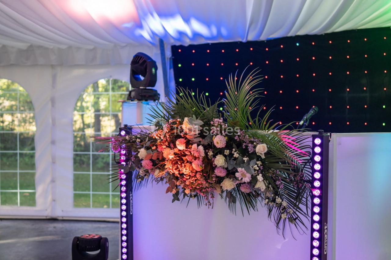 Table de DJ décorée de fleurs et éclairée par des lumières colorées sous une tente blanche.