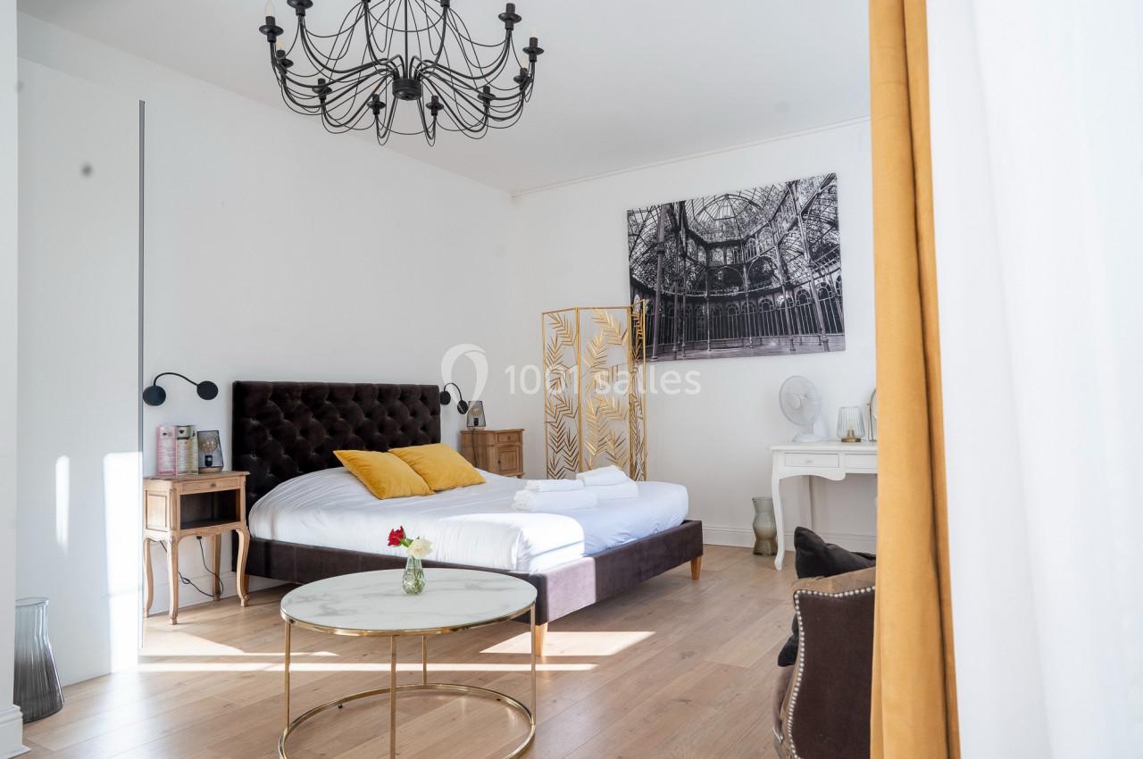 Chambre lumineuse avec lit double, coussins jaunes, mobilier en bois, table basse et décoration élégante.