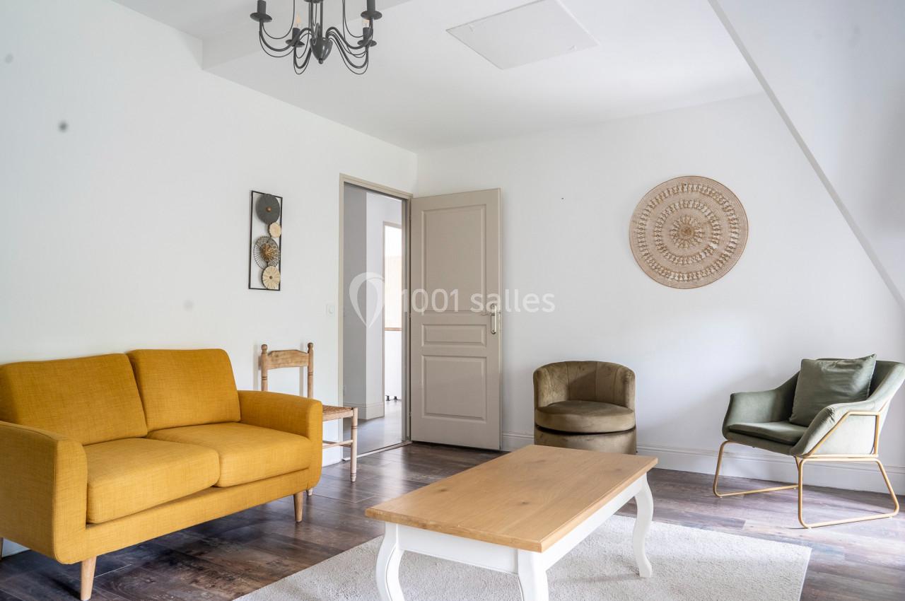 Salon lumineux avec canapé jaune, fauteuils, table basse en bois, parquet sombre et décoration murale.