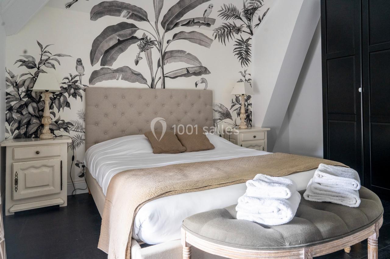 Chambre avec lit double, tête de lit capitonnée, mur décoré de motifs végétaux et mobilier classique clair.