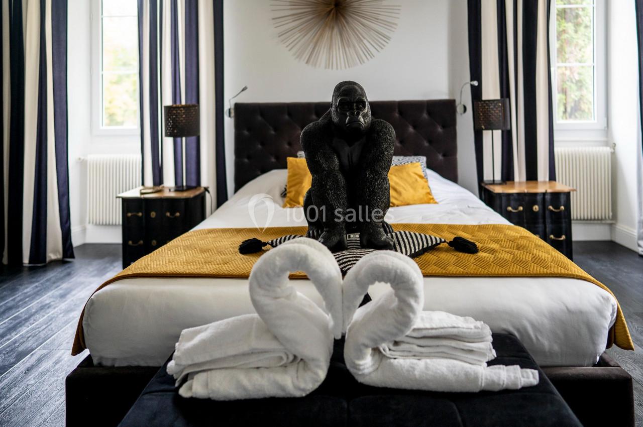 Lit double avec couvre-lit jaune, décoration de gorille noir au centre et serviettes pliées en forme de cygnes au premier…