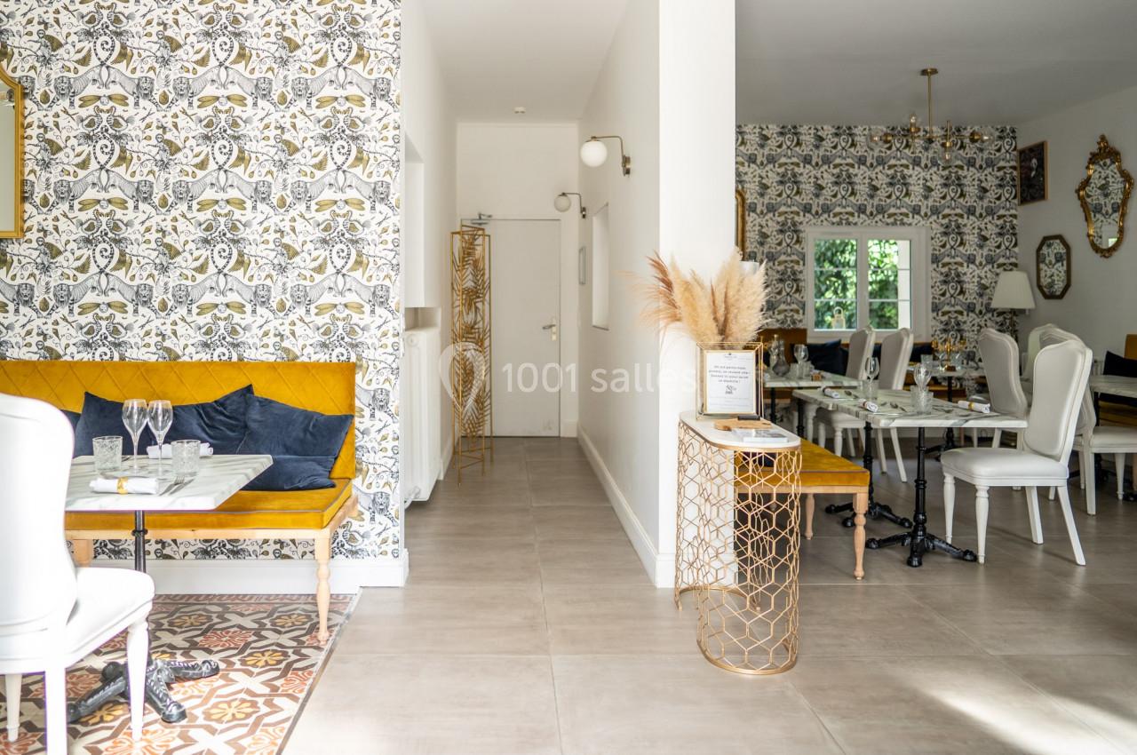 Salle lumineuse avec décoration élégante, murs ornés de papier peint à motifs, mobilier blanc et touches dorées.