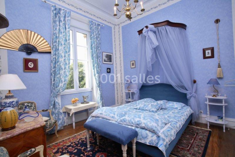 Chambre décorée dans des tons bleus avec lit à baldaquin, mobilier ancien et fenêtre donnant sur un jardin.