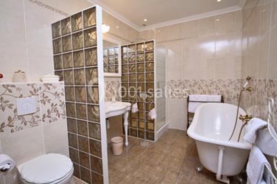 Salle de bain avec baignoire sur pieds, douche vitrée, lavabo, toilettes et carrelage beige décoré de motifs floraux.
