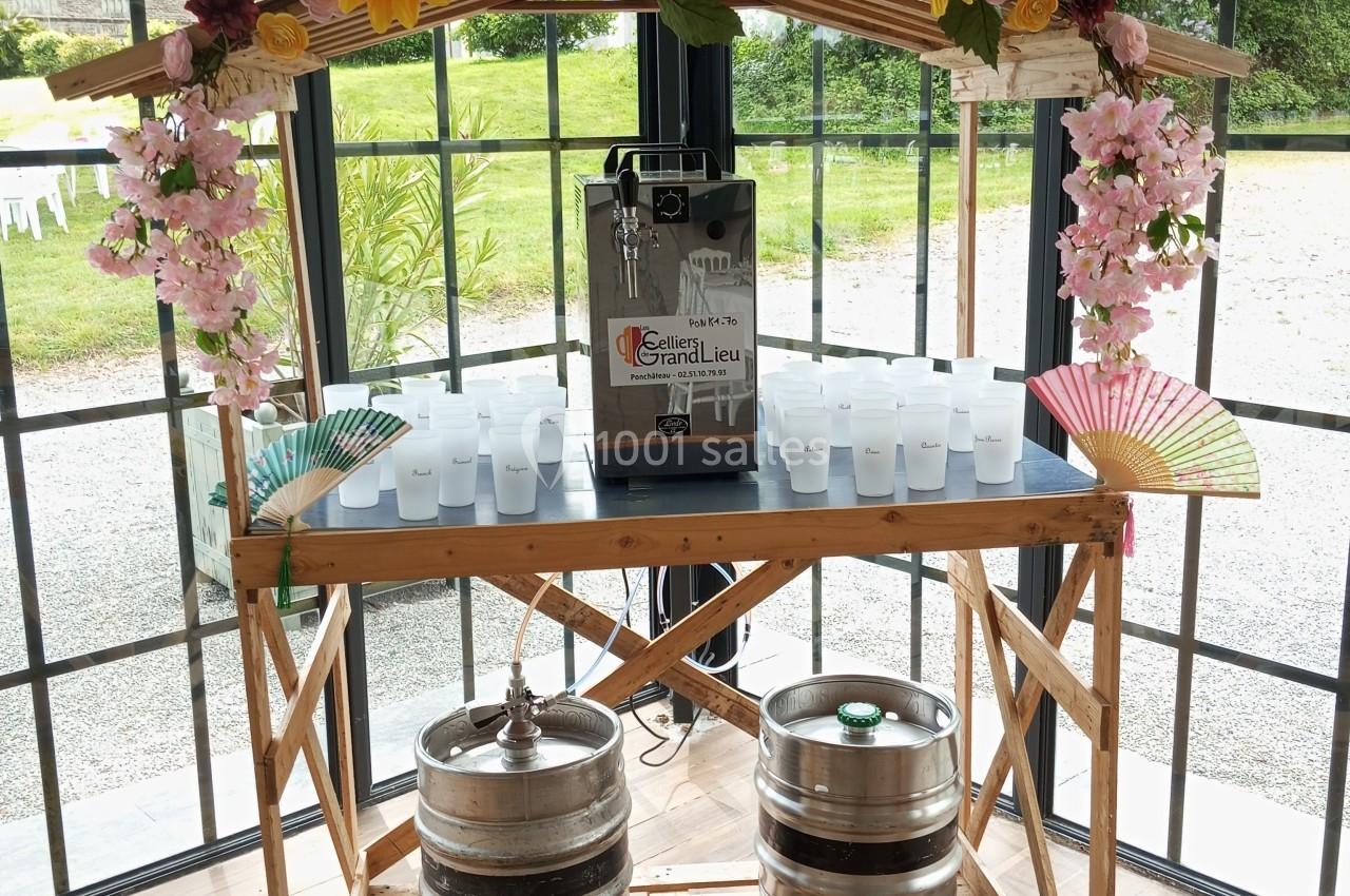 Stand en bois décoré de fleurs avec une tireuse à bière, des gobelets en plastique et des fûts dans un espace vitré.