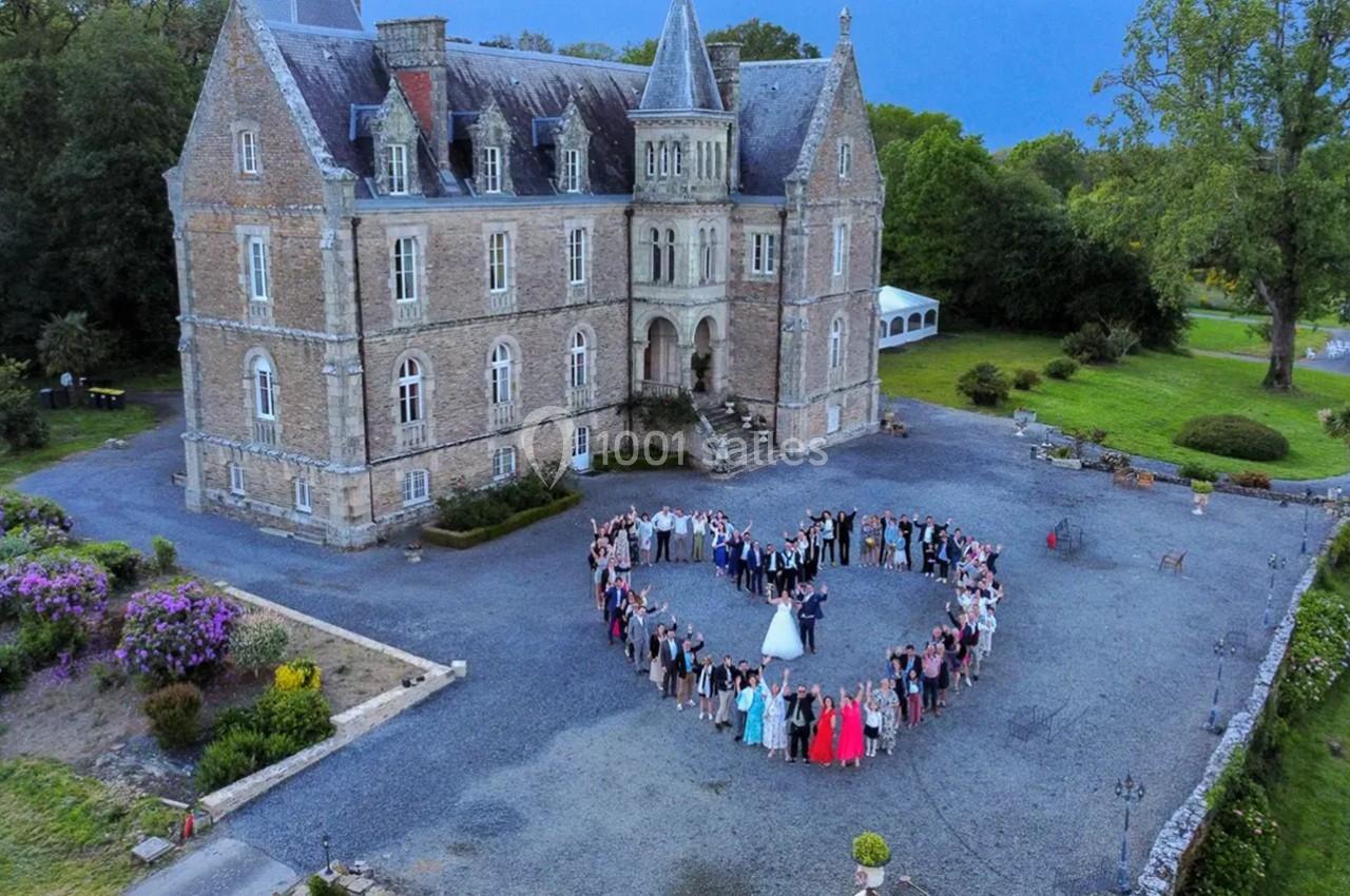 Vue aérienne d'un château entouré de verdure avec un groupe de personnes formant un cœur dans la cour.