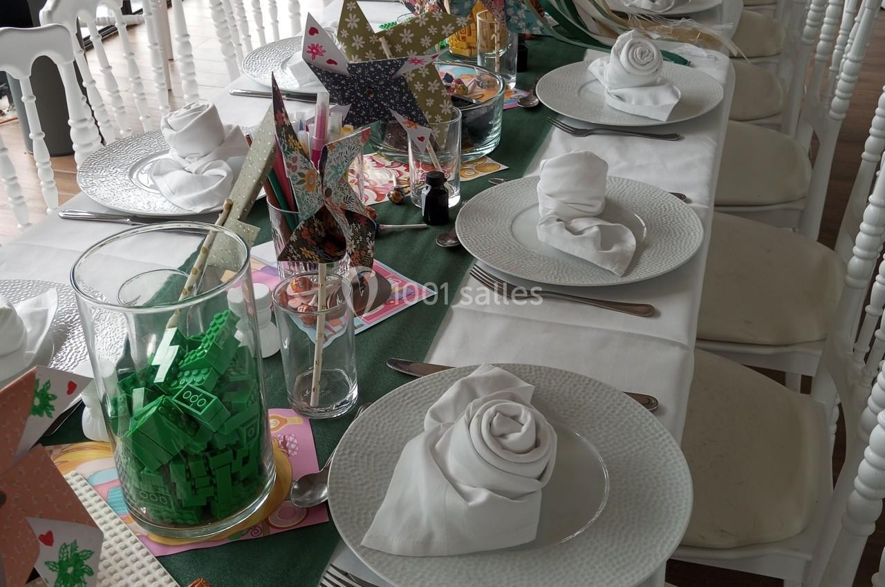 Table dressée pour un événement, avec nappes blanches, serviettes pliées, couverts et décorations colorées.