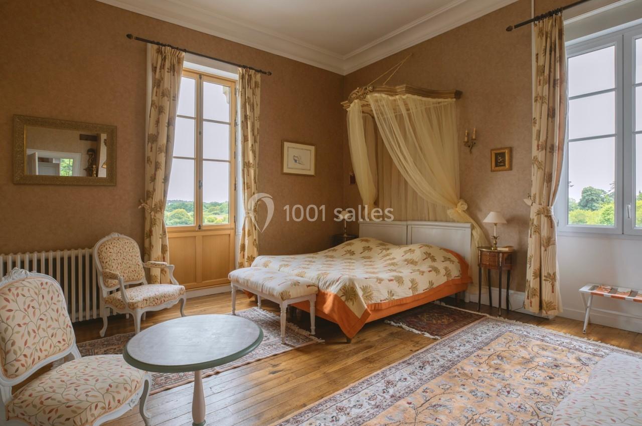 Chambre lumineuse avec lit à baldaquin, mobilier classique, parquet en bois et vue sur un paysage verdoyant.