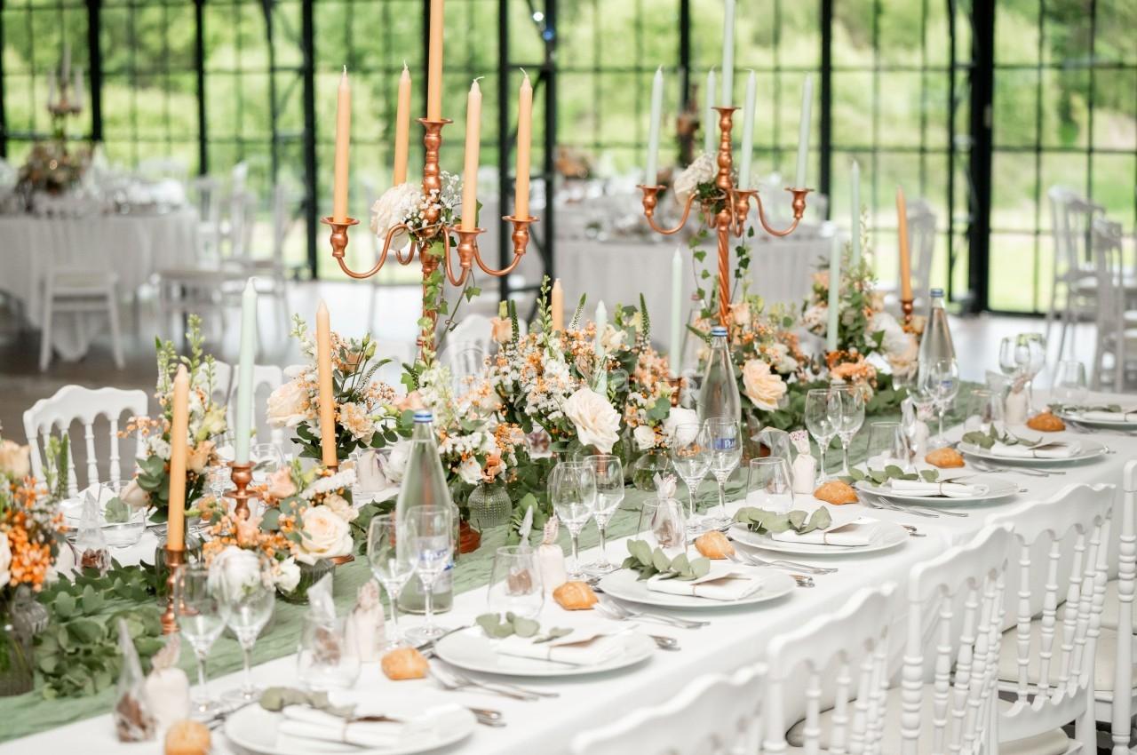 Table de réception élégamment dressée avec chandeliers dorés, fleurs fraîches et vaisselle raffinée dans une salle lumineuse.