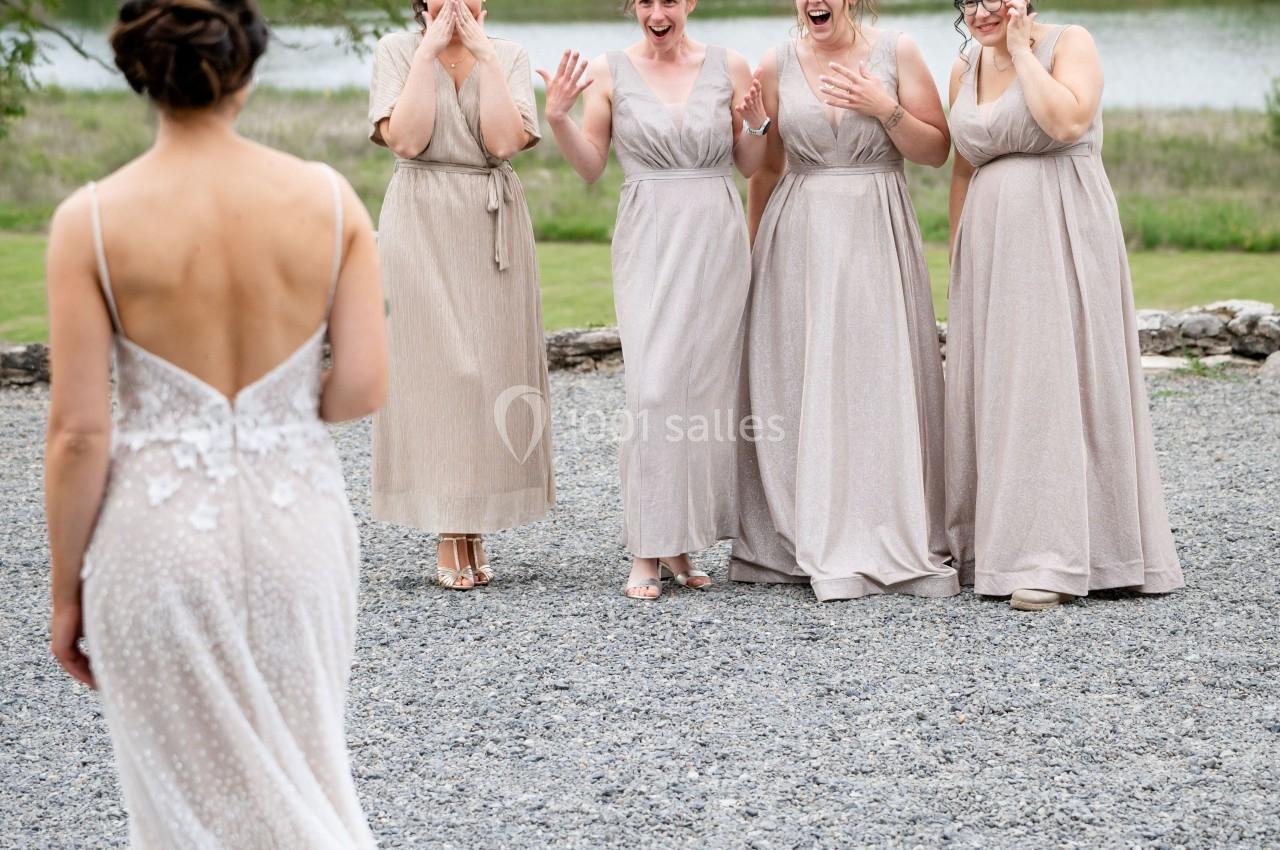 Une femme en robe de mariée fait face à quatre demoiselles d'honneur émues devant un paysage naturel.