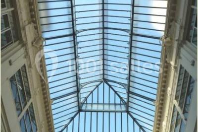 Plafond en verrière d'une galerie intérieure, laissant entrer la lumière naturelle sous un ciel dégagé.