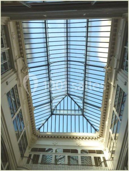 Plafond en verrière d'une galerie intérieure, laissant entrer la lumière naturelle sous un ciel dégagé.