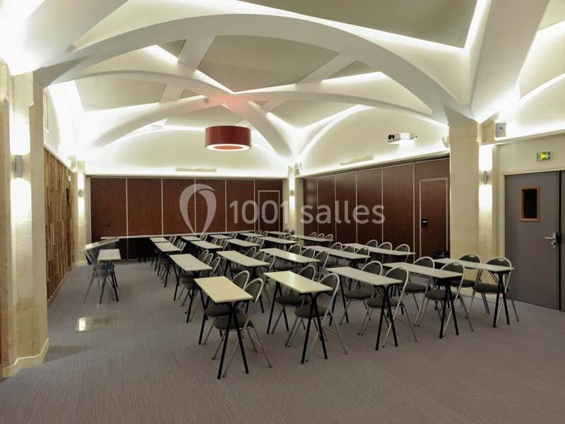 Salle de réunion moderne avec tables et chaises alignées, éclairage au plafond voûté et murs en panneaux boisés.