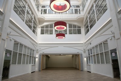 Vue intérieure d'une galerie lumineuse avec verrière, murs blancs et suspensions circulaires rouges.
